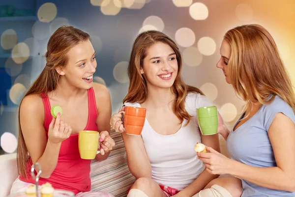 Mujeres jóvenes felices bebiendo té con dulces en casa — Foto de Stock