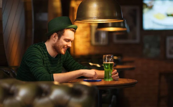 Человек со смартфоном и зеленым пивом в баре или пабе — стоковое фото