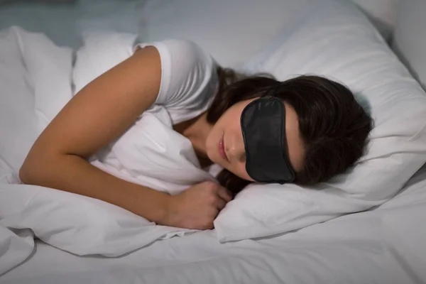 Mujer joven durmiendo con máscara ocular en la cama en casa —  Fotos de Stock