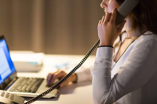 Woman with laptop calling on phone at night office — Stock Photo, Image