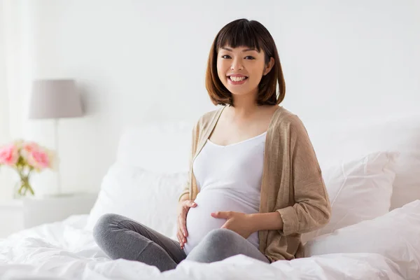 Glad gravid asiatisk kvinna sitter i sängen hemma — Stockfoto