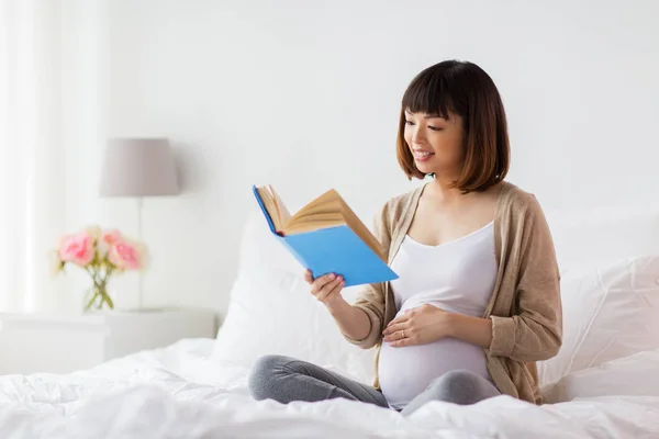 Feliz embarazada asiático mujer leyendo libro en casa —  Fotos de Stock