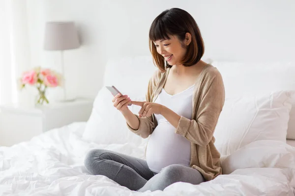 Gravid kvinna med smartphone i sängen hemma — Stockfoto