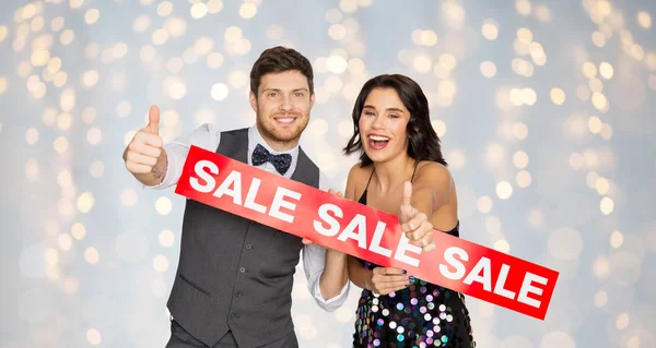 Casal feliz com sinal de venda vermelho mostrando polegares para cima — Fotografia de Stock