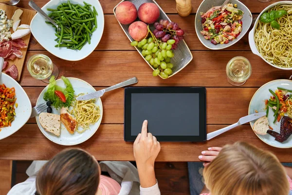 Mulheres com tablet pc na mesa cheia de alimentos — Fotografia de Stock