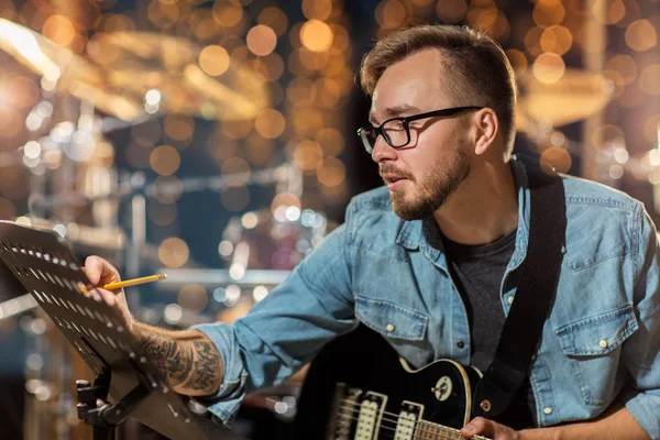 Hombre con escritura de guitarra a libro de música en el estudio — Foto de Stock