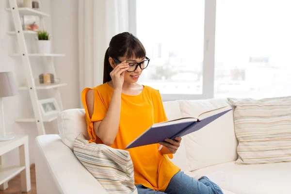 Giovane donna asiatica in occhiali lettura libro a casa — Foto Stock