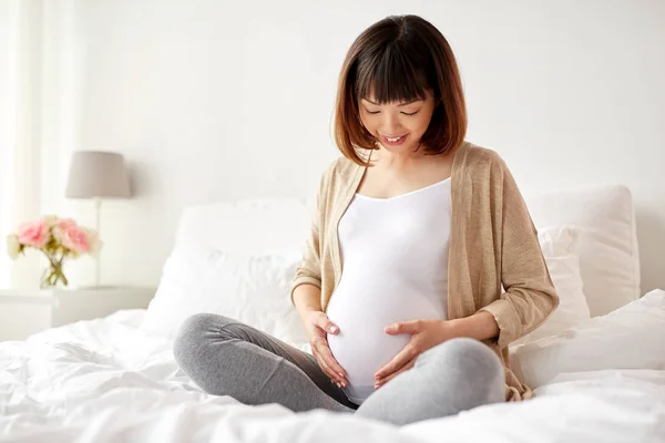 Felice donna asiatica incinta seduta a letto a casa — Foto Stock