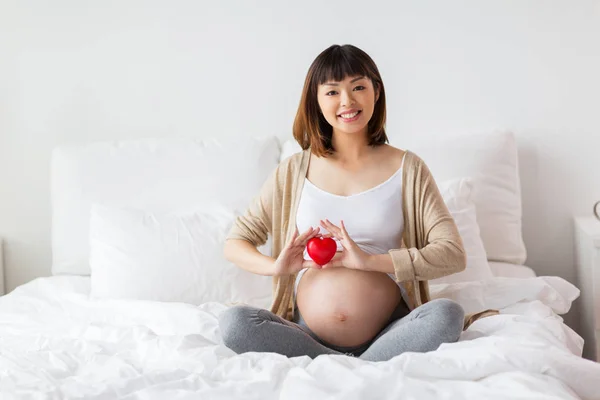 Glad gravid asiatisk kvinna med rött hjärta i sängen — Stockfoto