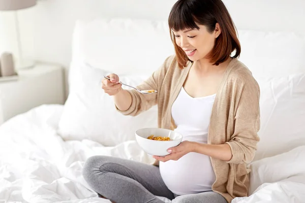 Happy pregnant woman eating cereal flakes at home — Stock Photo, Image