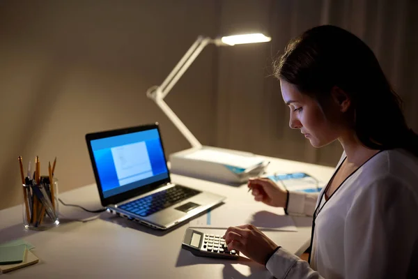 Mulher com calculadora e papéis no escritório da noite Fotos De Bancos De Imagens