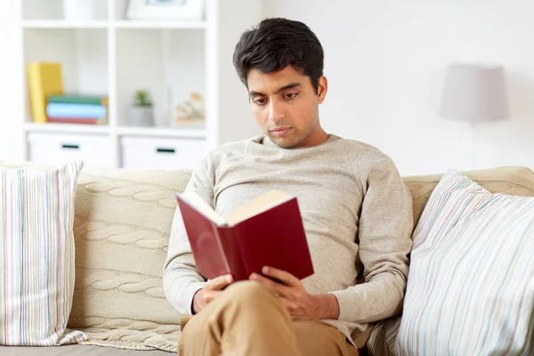 Homem sentado no sofá e livro de leitura em casa — Fotografia de Stock