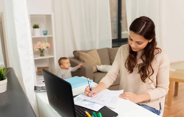 Madre feliz con el bebé y los papeles que trabajan en casa — Foto de Stock