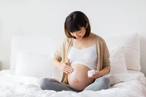 Happy asian pregnant woman applying cream to belly — Stock Photo, Image