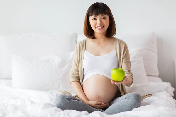Mulher grávida feliz com maçã na cama em casa — Fotografia de Stock