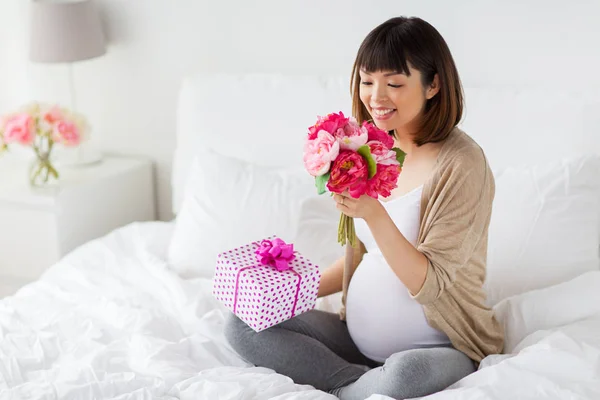 Счастливая азиатская беременная женщина с подарком и цветами — стоковое фото