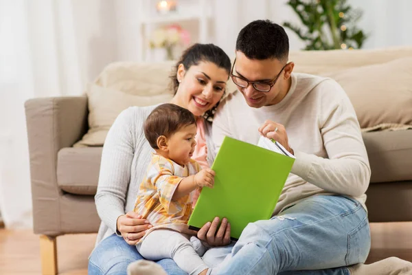 Família feliz com livro de leitura do bebê em casa — Fotografia de Stock