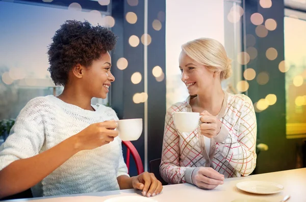 Happy young women drinking tea or coffee at cafe — Stock Photo, Image