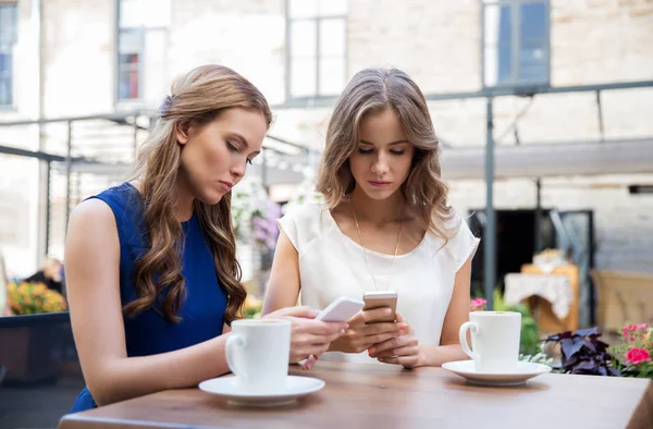Mujeres jóvenes con teléfonos inteligentes y café en la cafetería —  Fotos de Stock