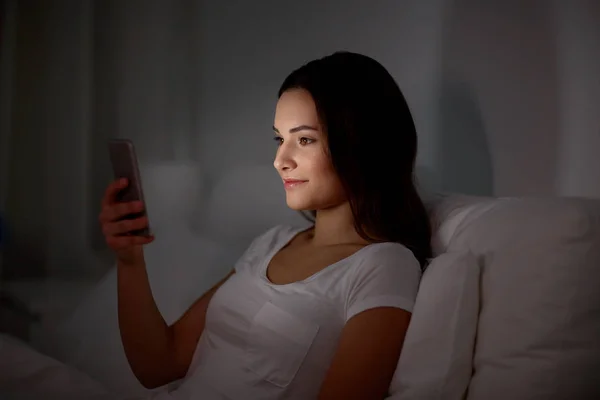 Счастливая молодая женщина со смартфоном в постели ночью — стоковое фото