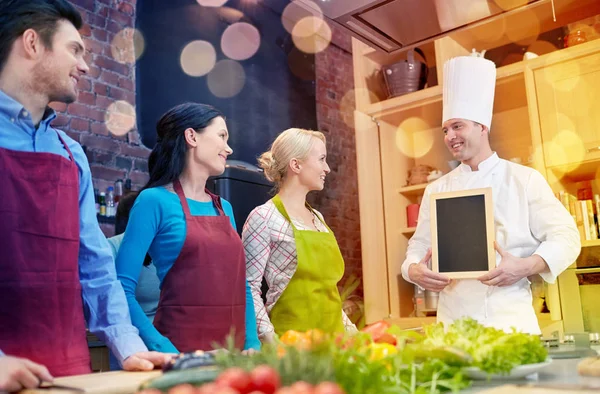 Amis heureux et chef cuisinier avec menu dans la cuisine — Photo