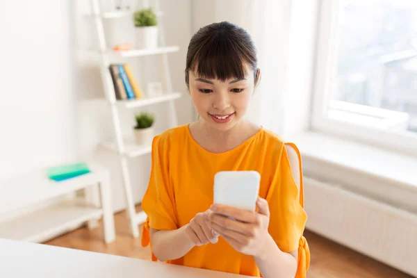Счастливая азиатка со смартфоном дома — стоковое фото