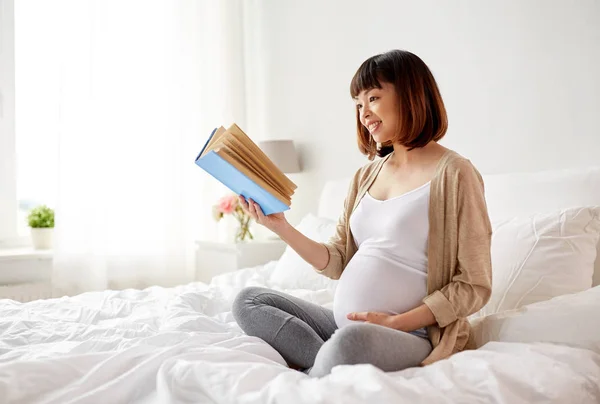 Щаслива вагітна азіатська жінка читає книгу вдома — стокове фото
