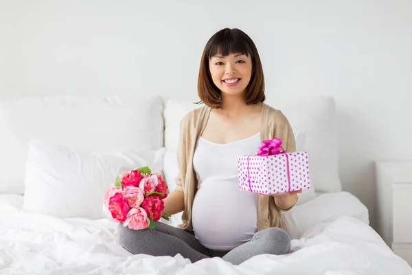 Lycklig asiatiska gravid kvinna med present och blommor — Stockfoto