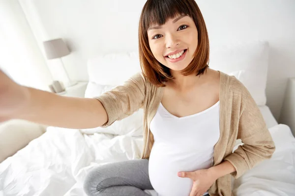 Kobieta w ciąży, biorąc selfie w łóżku w domu — Zdjęcie stockowe