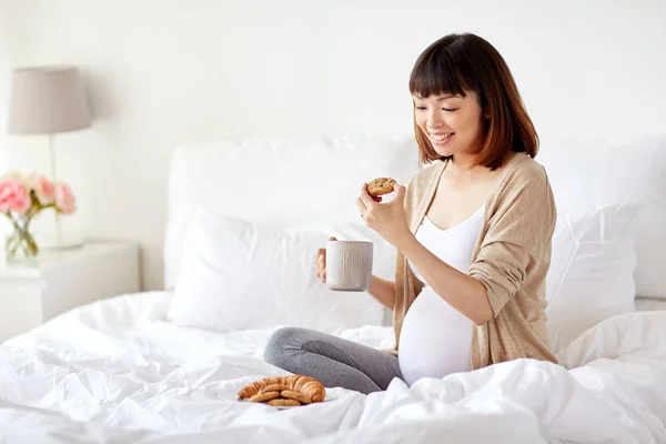 Evde yatakta çerez yemek mutlu hamile kadın — Stok fotoğraf