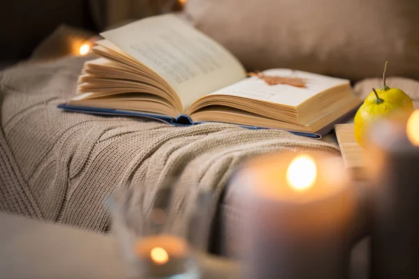 Libro con hoja de otoño y manta en el sofá en casa — Foto de Stock