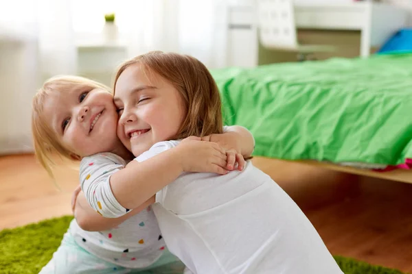 Glückliche kleine Mädchen oder Schwestern, die sich zu Hause umarmen — Stockfoto