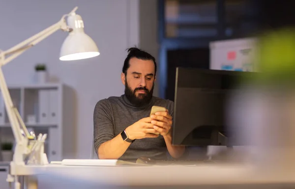 Creative man with smartphone at night office — Stock Photo, Image