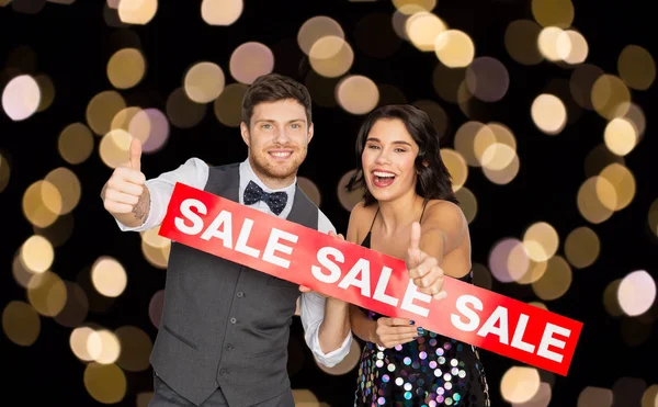 Щаслива пара з червоним знаком продажу, що показує великі пальці вгору — стокове фото