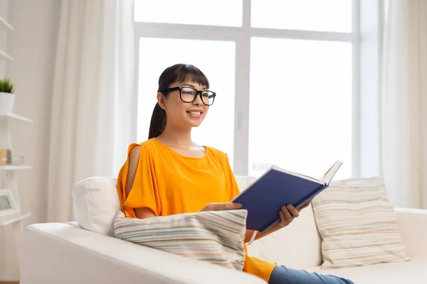 Mladá asijská žena v brýlích, čtení knihy doma — Stock fotografie