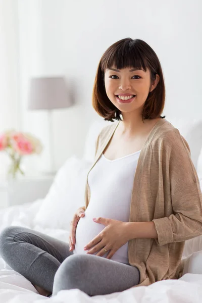 Feliz grávida asiática mulher sentada na cama em casa — Fotografia de Stock