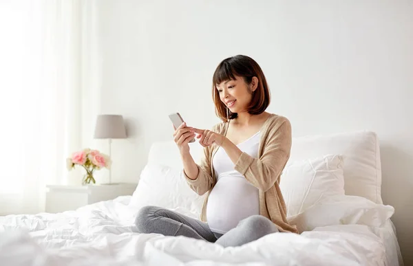 Donna incinta con smartphone a letto a casa — Foto Stock