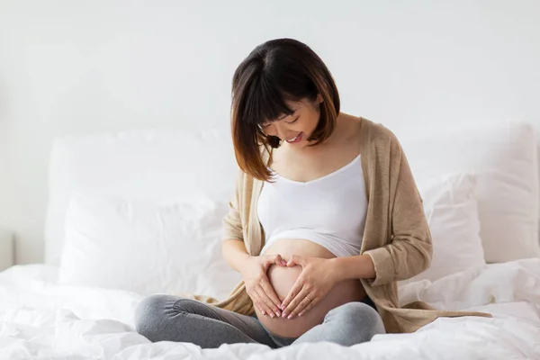 침대에서 행복 한 임신 여자 만드는 심장 제스처 — 스톡 사진