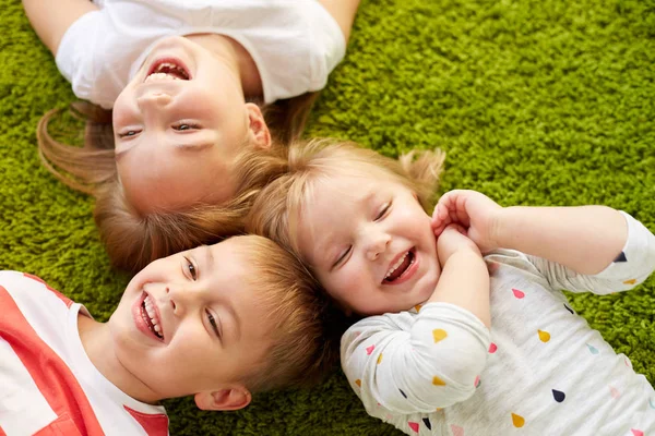 Niños pequeños y felices tumbados en el suelo o la alfombra —  Fotos de Stock