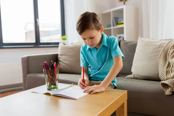 Мальчик с тетрадью и карандашами рисует дома — стоковое фото