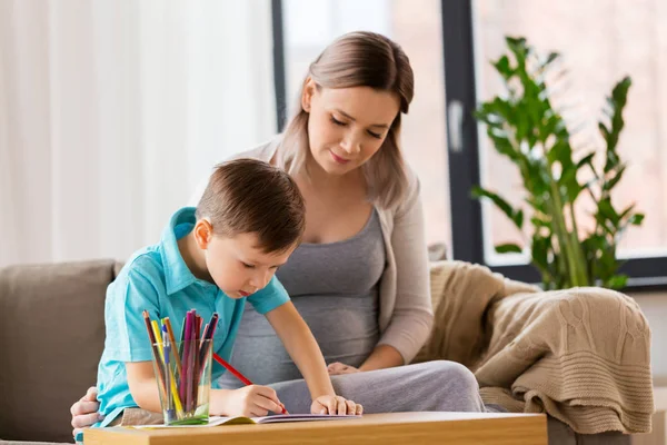 Schwangere Mutter und Sohn mit Arbeitsbuch zu Hause — Stockfoto