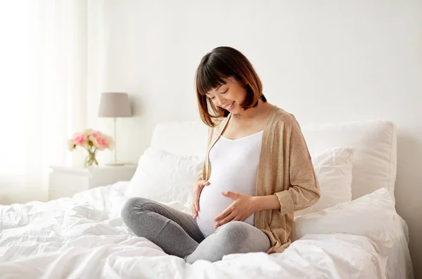 Felice donna asiatica incinta seduta a letto a casa — Foto Stock