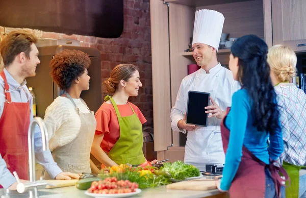 Gelukkige vrienden met chef-kok en tablet pc in keuken — Stockfoto