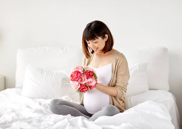 Glücklich asiatische schwangere Frau mit Blumen im Bett — Stockfoto