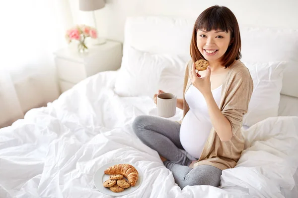 Mulher grávida feliz comer biscoito na cama em casa — Fotografia de Stock