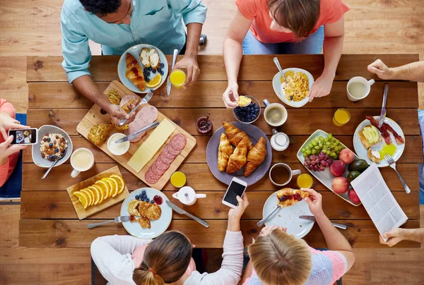 Люди со смартфонами едят еду за столом — стоковое фото