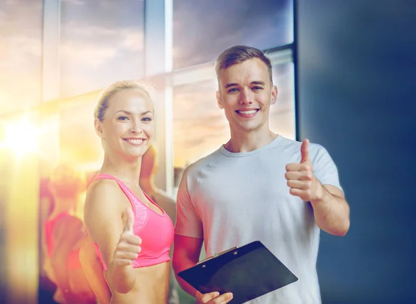 Sorrindo jovem mulher com personal trainer no ginásio — Fotografia de Stock