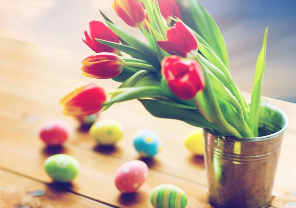 Tulipa flores em balde e ovos de Páscoa na mesa — Fotografia de Stock