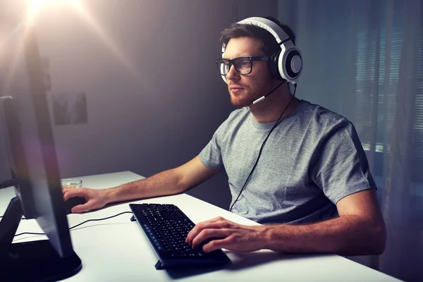 Ο άνθρωπος σε ακουστικά που παίζει το παιχνίδι γραφικών του υπολογιστή στο σπίτι — Φωτογραφία Αρχείου