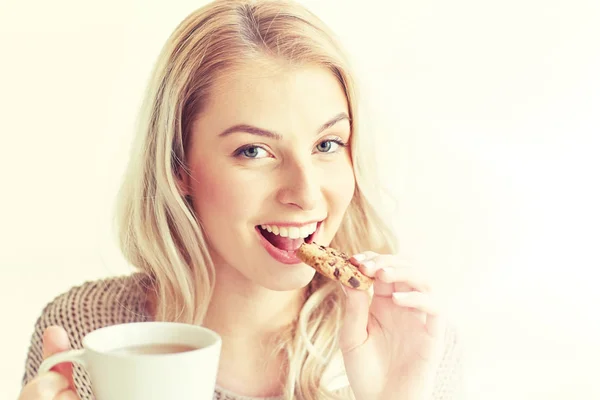 Lycklig kvinna med te äter cookie hemma — Stockfoto